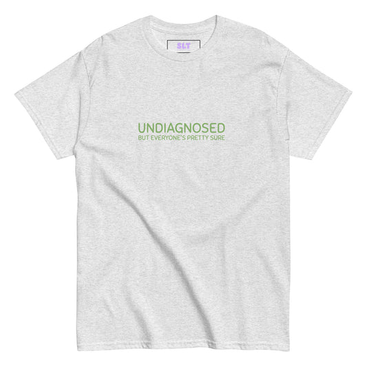 White t-shirt with “Undiagnosed But Everyone’s Pretty Sure” slogan, folded neatly on a lilac backdrop.