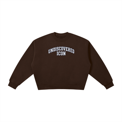 A dark brown cropped crewneck sweatshirt with 'UNDISCOVERED ICON' printed in white arched block letters across the chest, displayed flat against a solid white background.