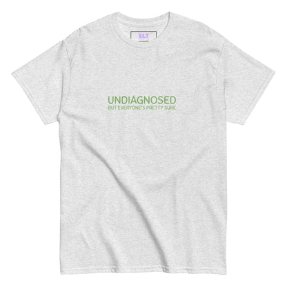 White t-shirt with “Undiagnosed But Everyone’s Pretty Sure” slogan, folded neatly on a lilac backdrop.